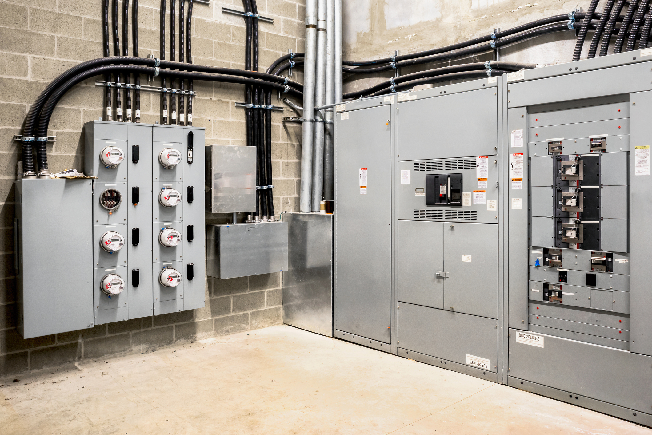 Commercial electrical room with utility meter banks, switchgear cabinets, and conduit on a block wall