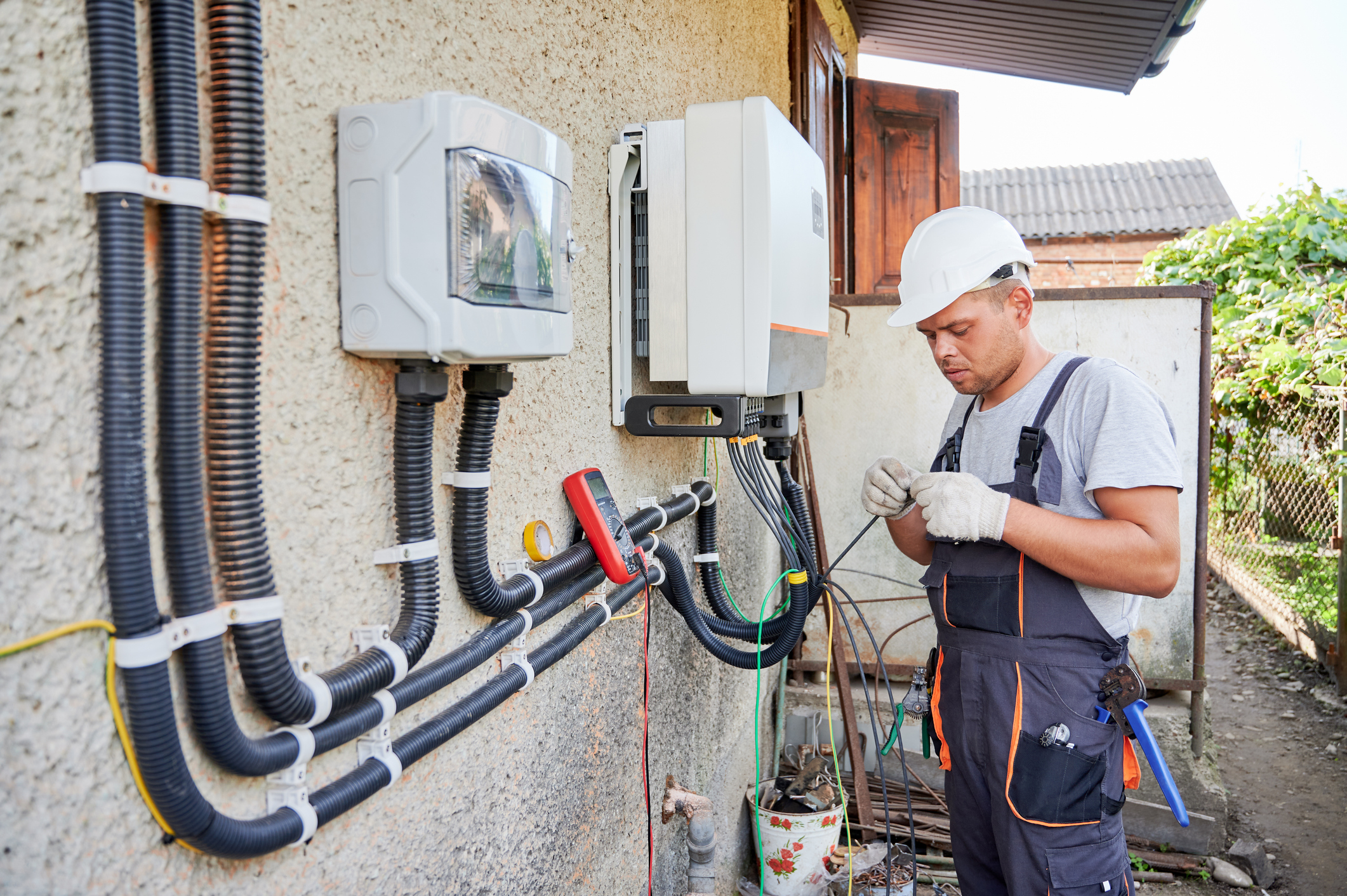 Electrician wiring an outdoor electrical transfer switch and connections on a building wall