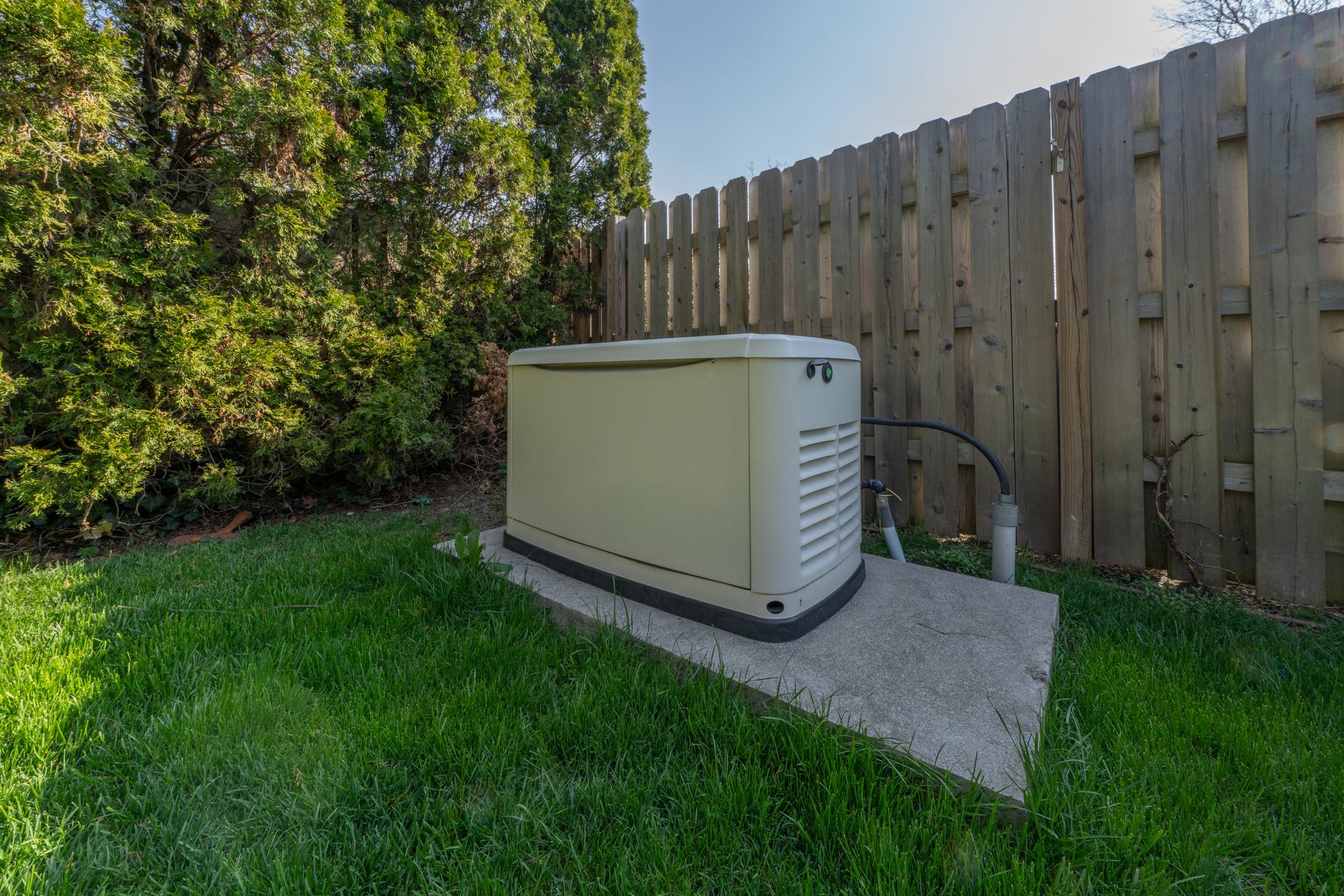 Residential standby backup generator on a concrete pad beside a backyard fence