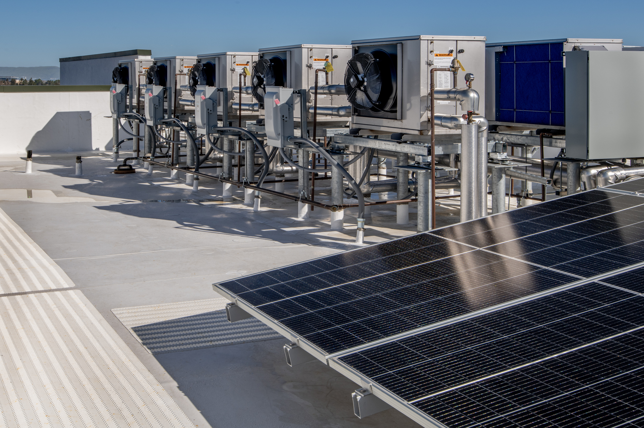 Rooftop commercial HVAC units and solar panels connected with electrical conduit and wiring