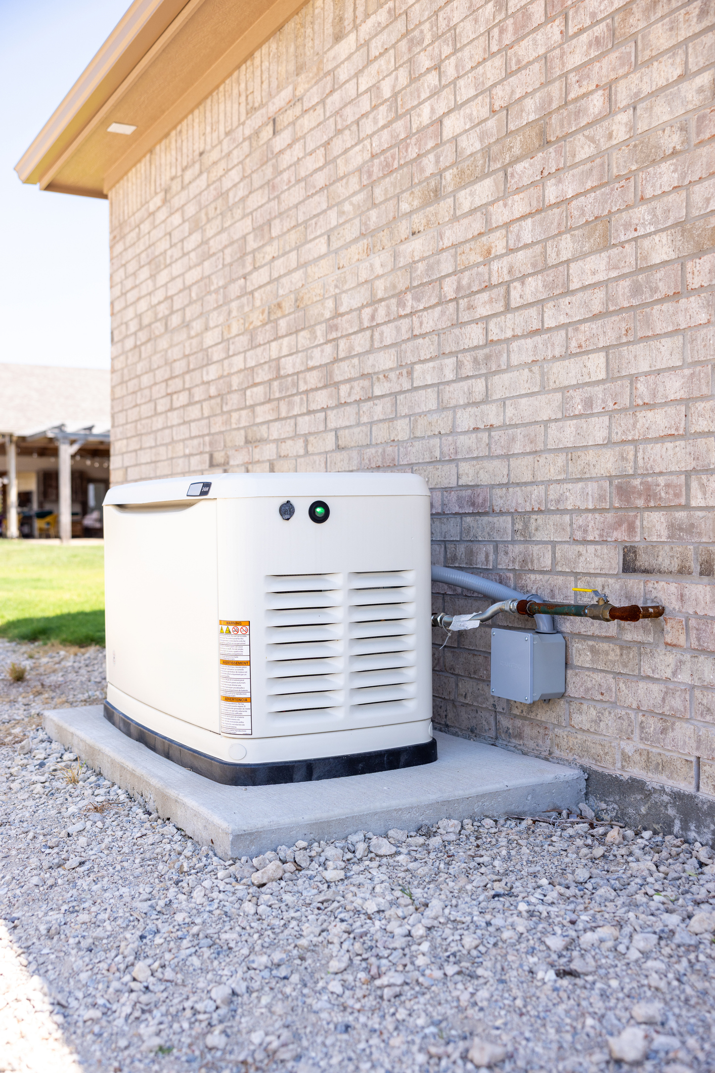 Standby generator installed on a concrete pad against a brick home with gas and electrical connections
