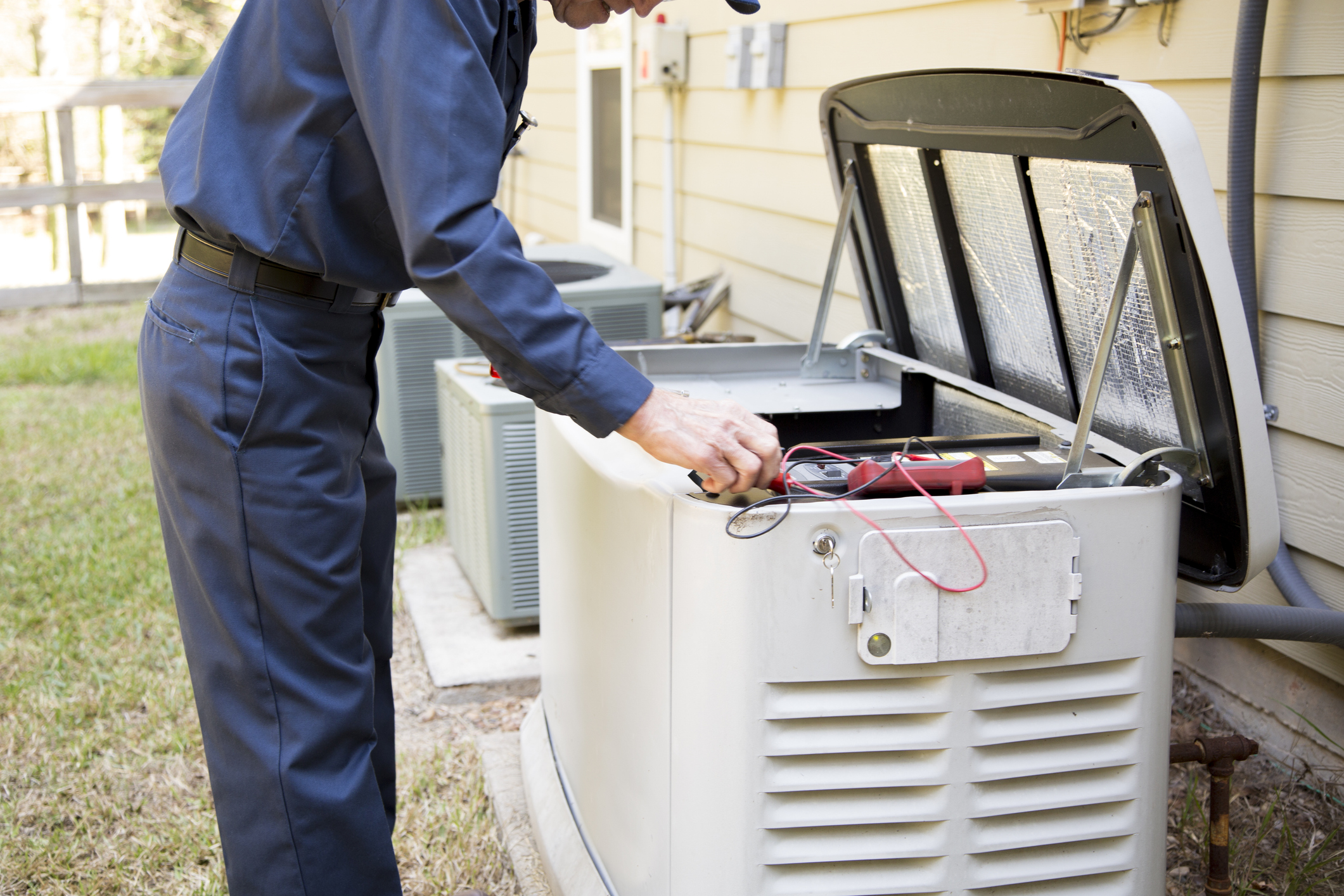 Technician servicing an open residential standby generator beside a home